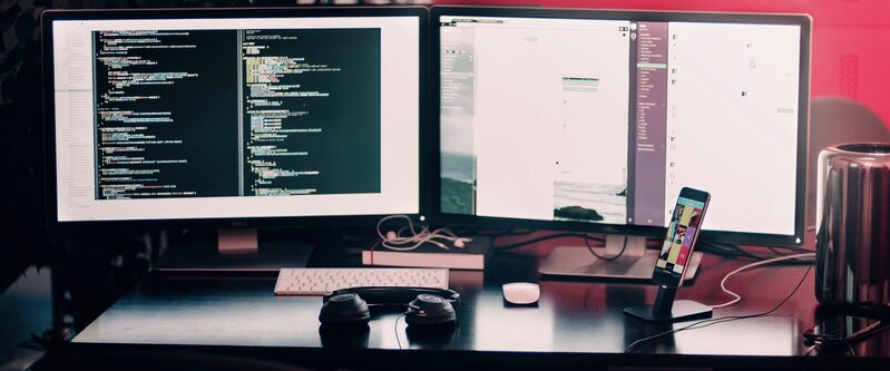 A developer's desk with code on two screens and a phone on a stand